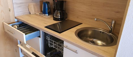 A compact kitchen with a dishwasher, a sink, a kettle, and a coffee maker.