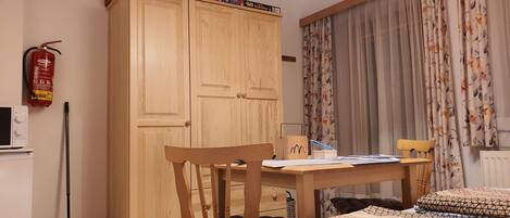Un dormitorio con un armario de madera, una mesa con papeles, una cama con ropa de cama estampada y un extintor en la pared.