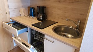 Een kleine keuken met een vaatwasser, een spoelbak, een waterkoker en een koffiezetapparaat.