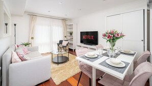 A modern living room with a sofa, a coffee table, a dining table set for two, and a TV displaying 'NETFLIX'. - Deluxe 2Bed Duplex w/parking (Greater London)