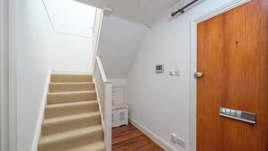 A staircase with beige carpet leading to a landing, a wooden door with a silver handle, and a small white storage unit in the background. - Deluxe 2Bed Duplex w/parking (Greater London)