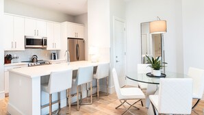 A modern kitchen with white cabinets, a stainless steel refrigerator, and a central island with bar stools. - SOCE FLATS 206 - Brand New Olde Naples Condo Steps to 5th Ave S! (Naples)