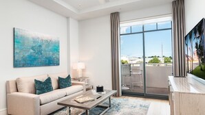 A modern living room with a beige sofa, a coffee table, and a large window with curtains. - SOCE FLATS 206 - Brand New Olde Naples Condo Steps to 5th Ave S! (Naples)