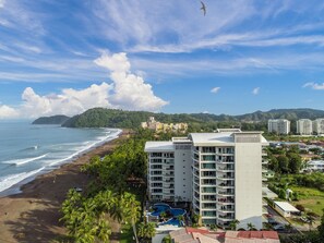 A beachfront hotel with a pool, ocean view, and a mountainous backdrop.