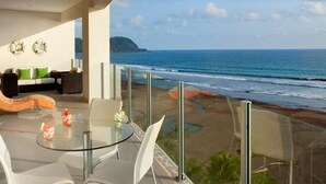 Un balcon avec une table et des chaises en verre, donnant sur une plage et l’océan.