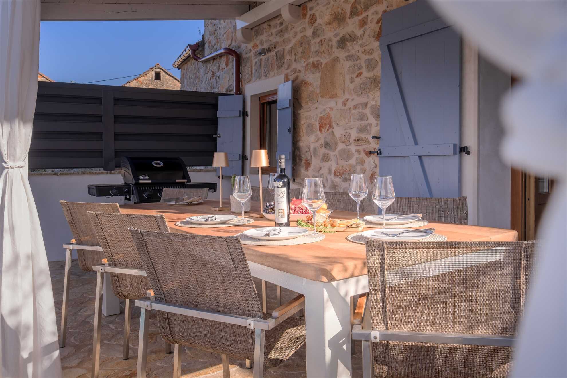 An outdoor dining area with a stone wall, a grill, and wicker chairs.
