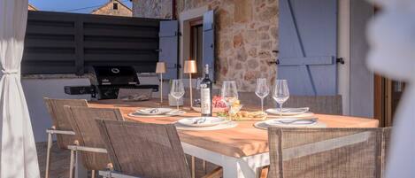 An outdoor dining area with a stone wall, a grill, and wicker chairs.