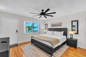 A modern bedroom with a bed, bedside tables, a ceiling fan, a window with a view, and a door. - 7th Heaven 1 Bedroom Condo by RedAwning (Longboat Key)
