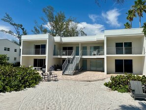 A modern multi-story building with a central staircase, outdoor seating, and a sandy courtyard. - 7th Heaven 1 Bedroom Condo by RedAwning (Longboat Key)