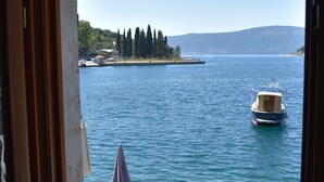 A view from a balcony with a stone railing, overlooking a calm lake with a small boat and a distant island. - Villa Serventi, Apartment with Sea View Balcony (Tivat)