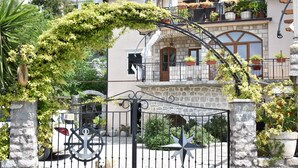A stone gate with a metal fence, a dog, and a white car parked nearby. - Villa Serventi, Apartment with Sea View Balcony (Tivat)