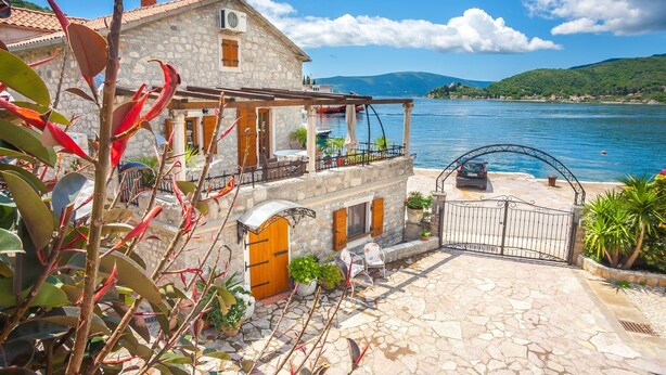 A stone house with a balcony overlooking a lake, a gate, and potted plants. - Villa Serventi, Apartment with Sea View Balcony (Tivat)