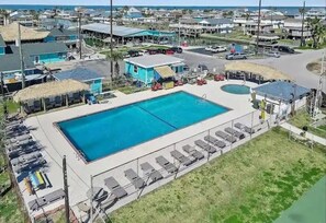 Uma piscina retangular grande com cadeiras de sol e guarda-sóis, cercada por uma grade.