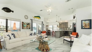 A spacious living room with a white sofa, a glass coffee table, and a dining area with a kitchen in the background.