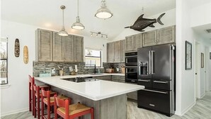 A modern kitchen with a large island, stainless steel appliances, and red bar stools.