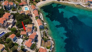 Luchtbeeld van een kustgebied met woonhuizen, een strand en helder turquoise water.