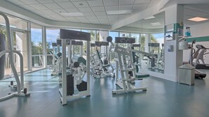 Een fitnessruimte met diverse trainingsapparaten, grote ramen en uitzicht op palmbomen.
