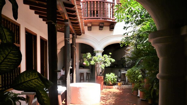 A courtyard with a central white circular structure, surrounded by potted plants and a wooden pergola.