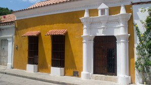 A yellow building with a tiled roof, white columns, and a wooden door.