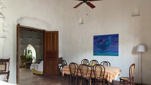 A dining area with a table set for four, surrounded by wicker chairs, a ceiling fan, and a painting of a bird on the wall.