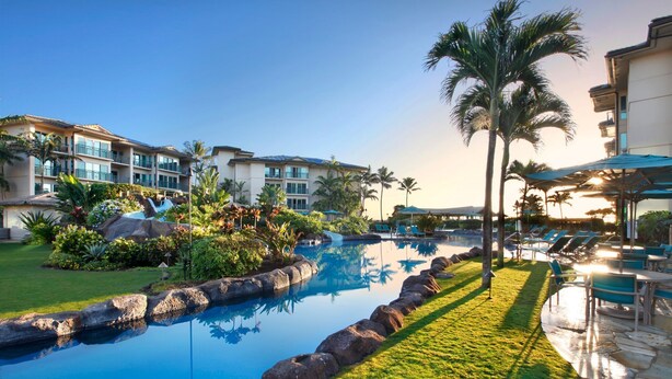 A resort with a swimming pool, palm trees, and a building with balconies. - Waipouli Beach Resort Condo Perfect for Families or Quiet Getaway! (Kapaa)