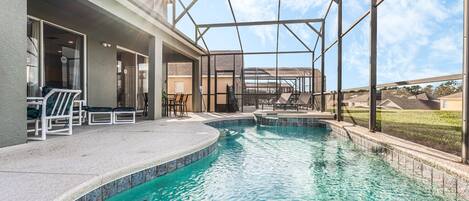 A swimming pool with a covered area, outdoor seating, and a view of the surrounding landscape.
