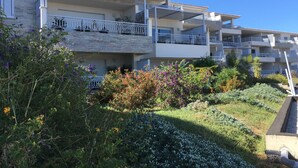 Un immeuble résidentiel à plusieurs étages doté de balcons, d’un espace jardin avec différentes espèces de plantes et d’un ciel bleu dégagé.