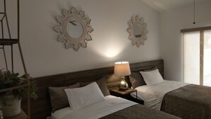 Quarto de hotel com duas camas, uma mesa de cabeceira com abajur, espelhos decorativos na parede e uma planta.