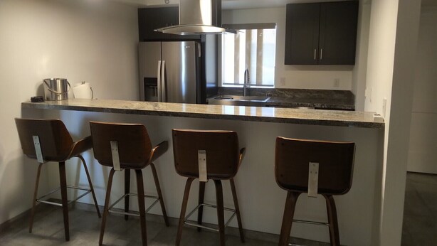 Cozinha moderna com ilha central, eletrodomésticos de aço inoxidável e banquetas.