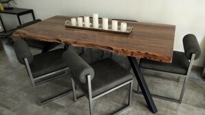 Uma mesa de jantar com tampo de madeira e pernas de metal, acompanhada por quatro cadeiras estofadas.