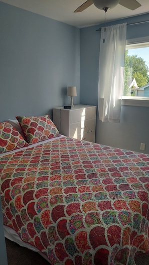 A bedroom with a bed, a nightstand, a lamp, and a window with curtains.