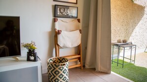 Quarto com televisão, cadeira de madeira, toalha branca, cesta de palha e pequena mesa com objetos decorativos.