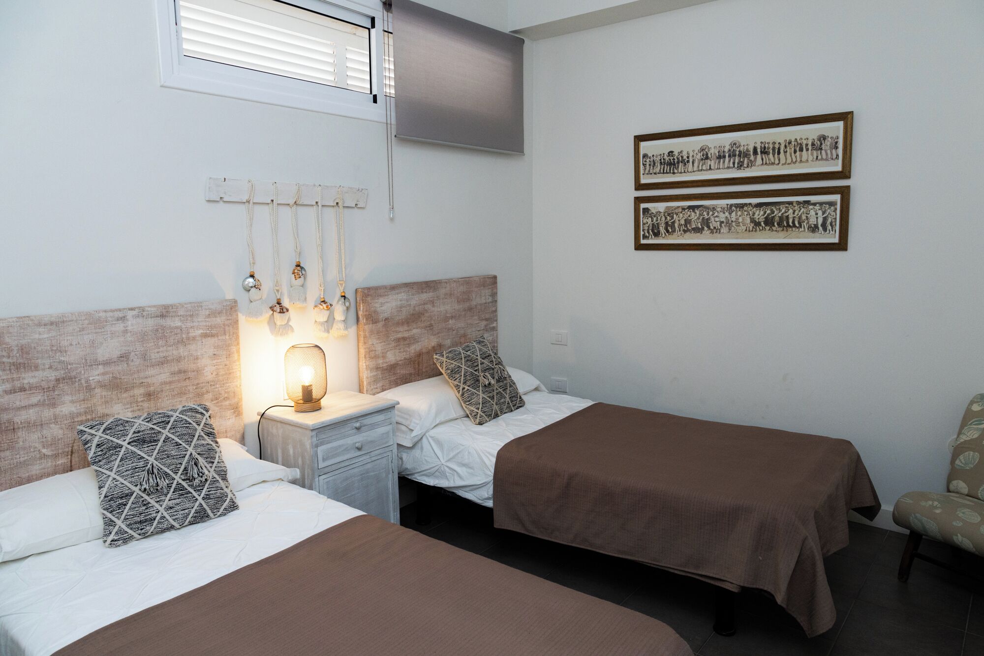 A room with two beds, a nightstand with a lamp, and two framed photographs on the wall.