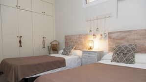 Quarto com duas camas, uma mesinha de cabeceira com luminária, cabeceira de madeira e um guarda-roupa com espelho.