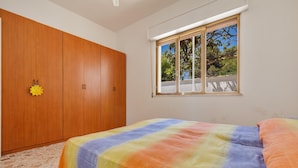 Een slaapkamer met een grote kast, een bed met een kleurrijke sprei en een raam met uitzicht op bomen.