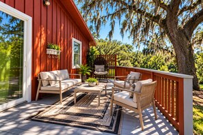 A red wooden deck with outdoor furniture, a swing chair, and a view of trees and sky.