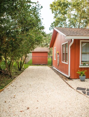 A gravel path leading to a red wooden building with a window and a door.