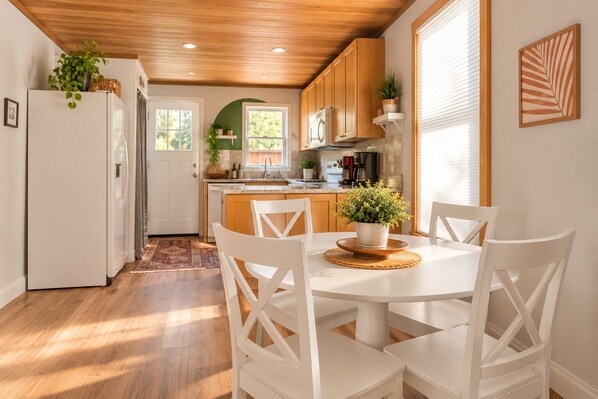 Una cocina moderna con armarios blancos, una mesa de comedor con sillas y una planta en maceta sobre la mesa.