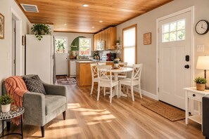 A modern kitchen with white cabinetry, a dining area with white chairs, and a cozy seating area with a grey sofa.