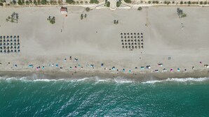Une vue aérienne d’une plage avec des rangées de parasols et de chaises de plage, une tour de surveillance et un petit bâtiment.