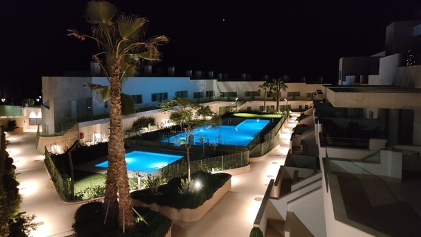 Un hôtel moderne doté d’une piscine, de palmiers et d’un espace extérieur bien éclairé la nuit.