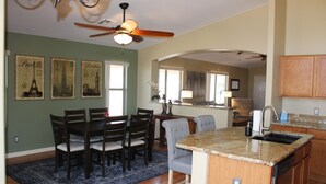 A dining area with a wooden table and chairs, a kitchen with granite countertops, and a ceiling fan. - Private Heated Pool in Apache Junction (Apache Junction)