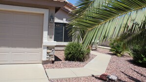 A residential house with a garage, a stone pillar, and a well-maintained garden with palm trees and shrubs. - Private Heated Pool in Apache Junction (Apache Junction)