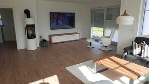 A modern living room with a wooden floor, a TV, a sofa, a coffee table, and a fireplace. - New, exclusive vacation home close to the beach with sauna, 3 bedrooms, fireplace, garage, (Dranske-Lancken)