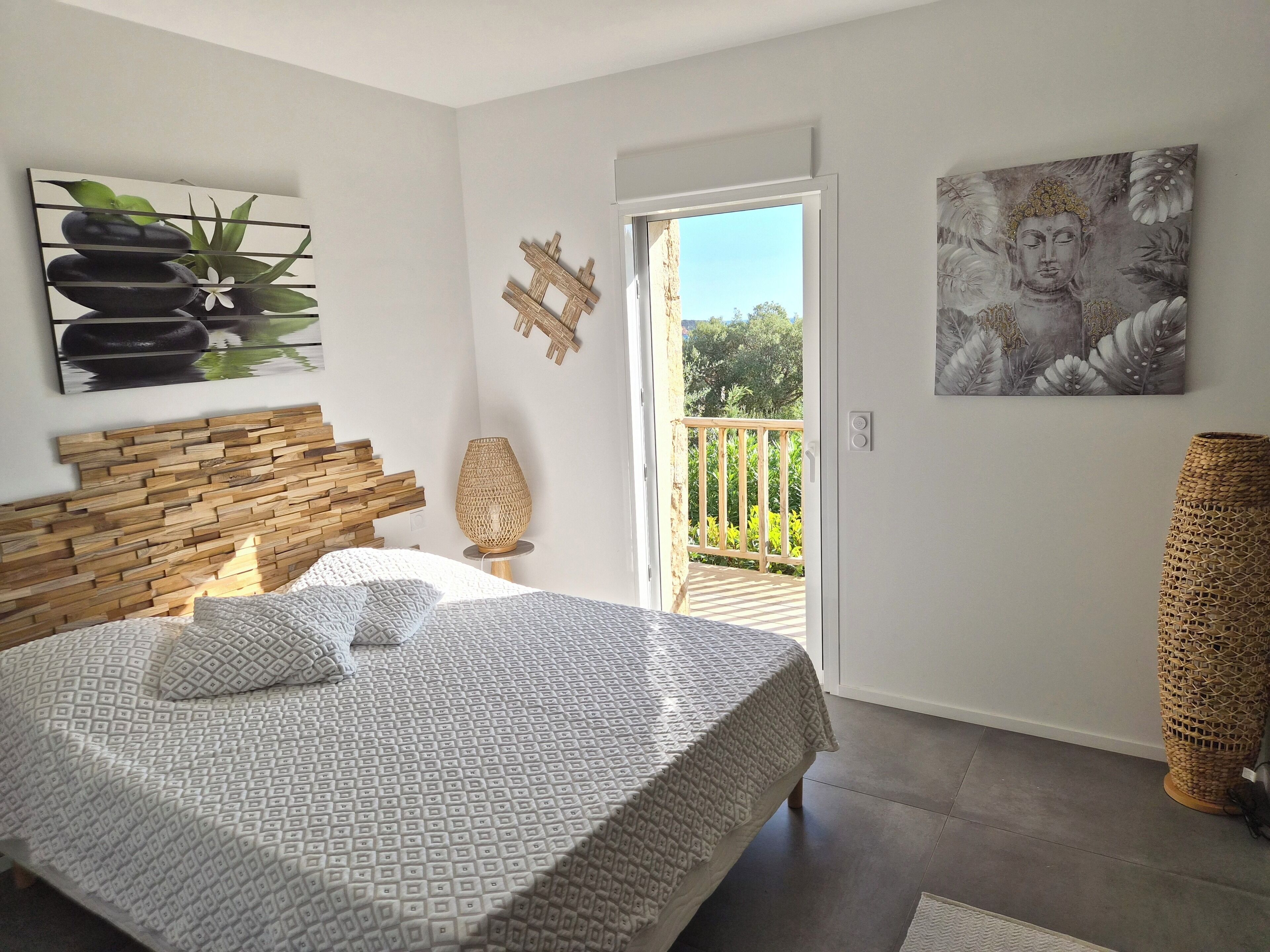Une chambre à coucher avec un lit, une tête de lit en bois, une grande fenêtre et un balcon.