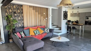 Un salon moderne avec un canapé gris, une table basse ronde et un escalier menant à un espace cuisine.