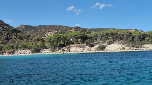 Une plage côtière aux eaux d’un bleu limpide, bordée de collines verdoyantes.