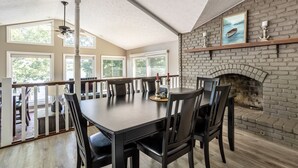 A dining area with a brick fireplace, large windows, and a wooden table. - Lakeside Cottage w/ Spacious Multi-level Deck and Outdoor Living Space (Monticello)
