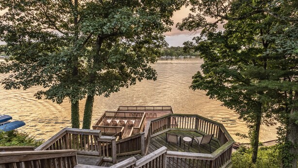 A wooden deck with multiple seating areas overlooking a river. - Lakeside Cottage w/ Spacious Multi-level Deck and Outdoor Living Space (Monticello)