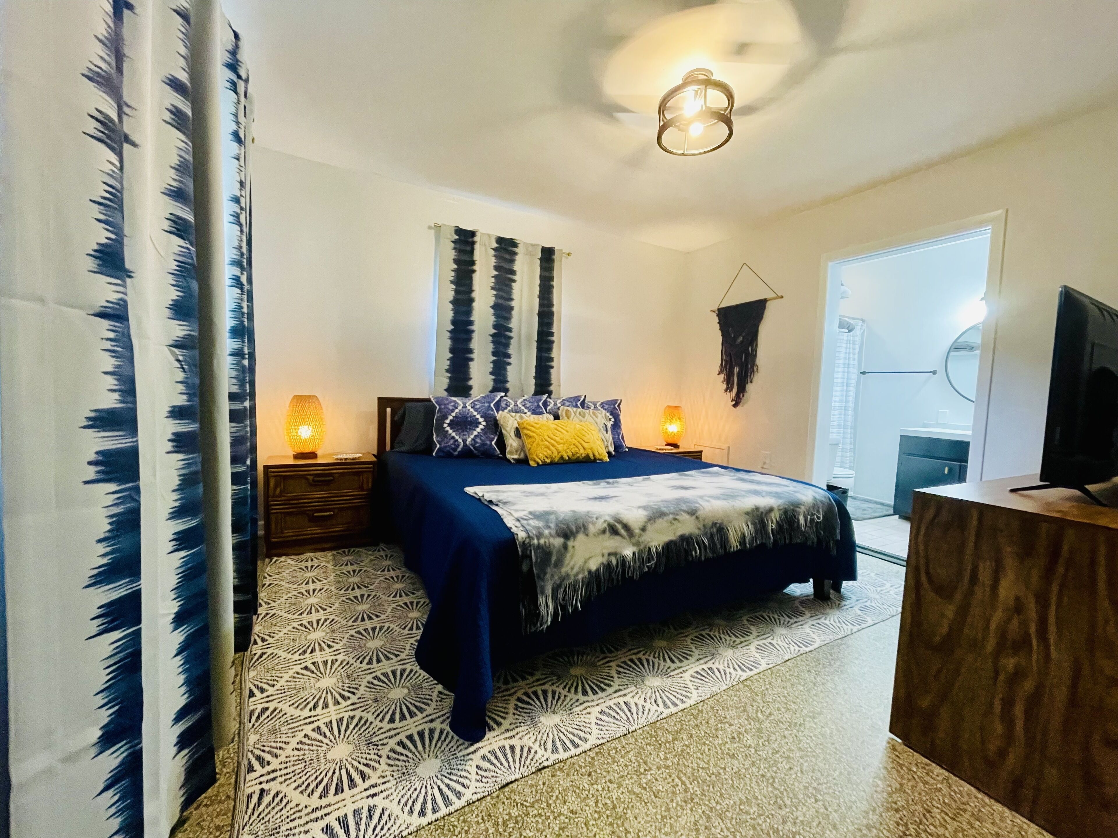 Une chambre à coucher avec un lit, deux tables de chevet avec des lampes, une tapisserie murale et un téléviseur posé sur un meuble en bois.